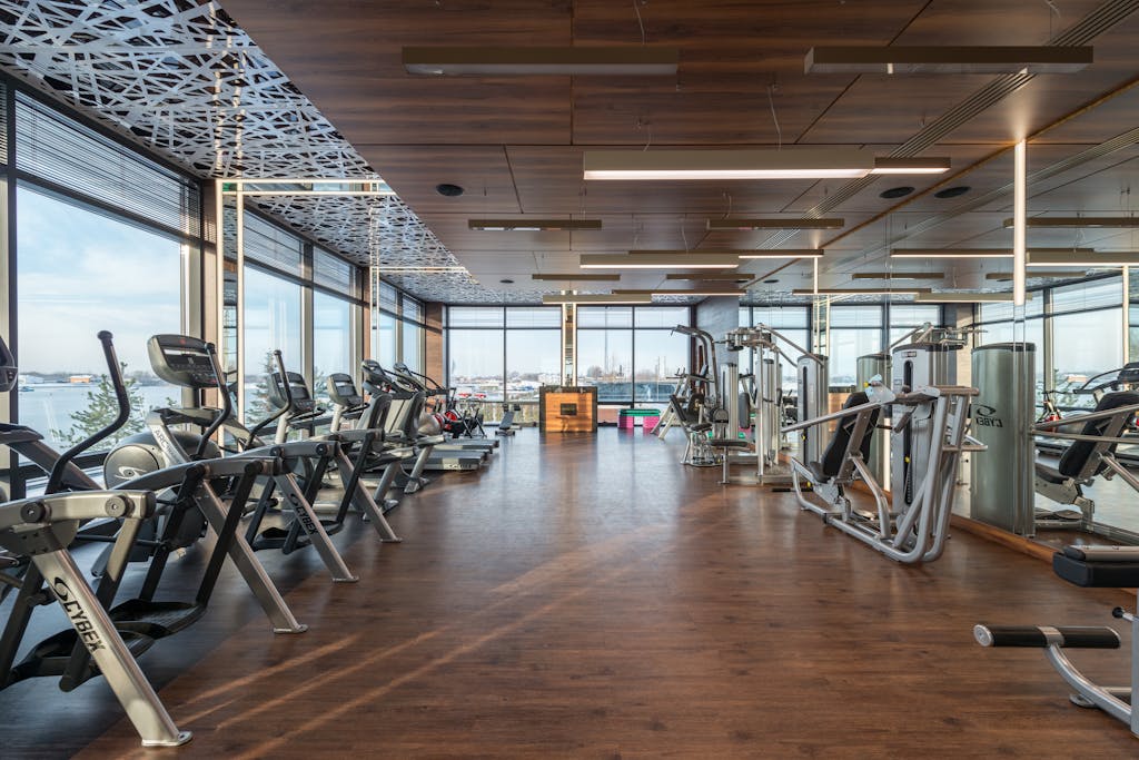 Interior of modern spacious fitness club with various sports machines and equipment placed on parquet floor near panoramic windows